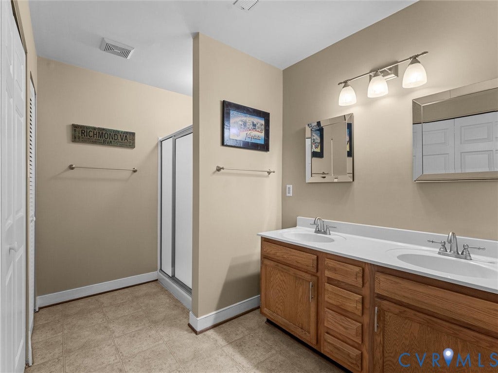 12100 English Ivy Lane, Glen Allen, VA 23059 Double-vanity cabinet with wood-finish cabinetry, solid-surface countertop with integrated dual sinks, chrome fixtures, and dual framed wall-mounted mirrors