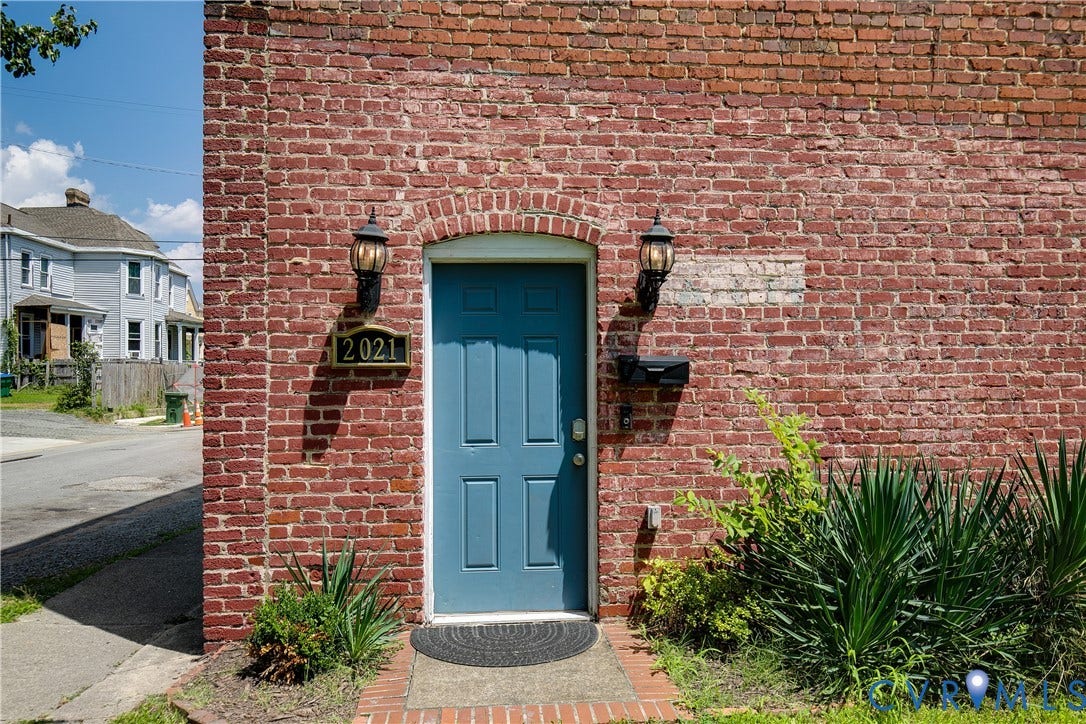 2021 North Avenue, Richmond, VA 23222 Brick exterior featuring an arched doorway with a blue door, two exterior sconces, a mailbox, and address numbering