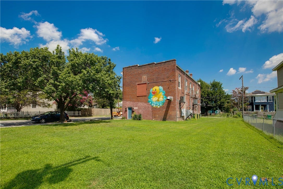 2021 North Avenue, Richmond, VA 23222 Expansive green space with a chain-link fence, mature trees, and a brick exterior building