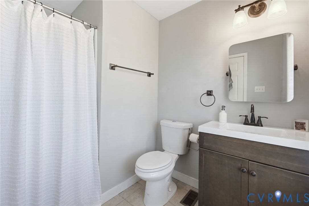 3015 M Street, Church Hill, Richmond, VA 23223 Bathroom featuring a wood-finish vanity with an integrated sink, a rounded rectangular mirror, and a two-light vanity fixture