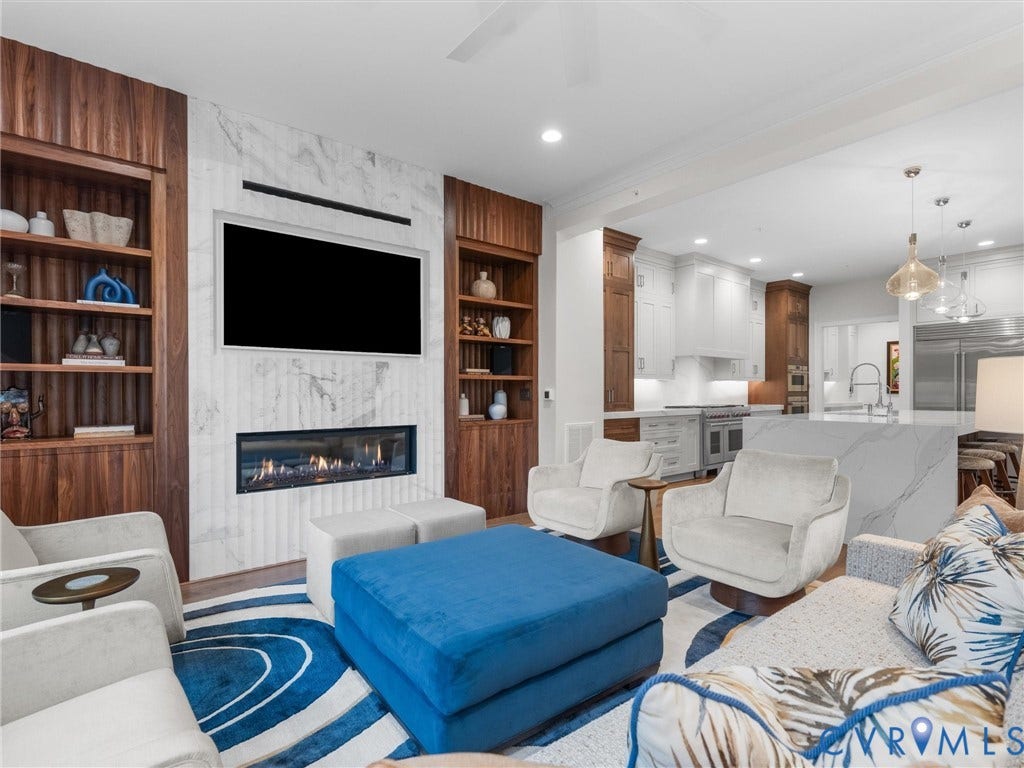 511 Libbie Avenue, #A, The Row At Westhampton, Richmond, VA 23226 Living area featuring a linear fireplace set within a marble-clad wall, flanked by built-in wood shelving, with a kitchen beyond featuring white cabinetry and a large island with a waterfall countertop