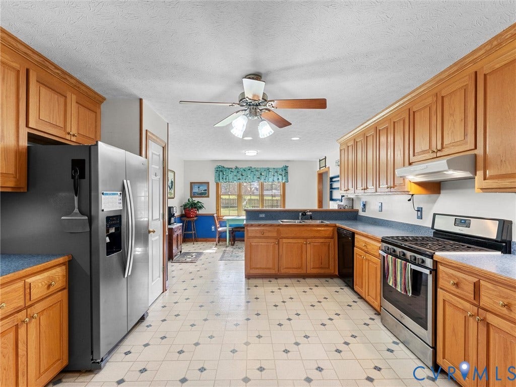 5325 Swift Hill Lane, Scandia Lake, Sandston, VA 23150 Expansive kitchen featuring wood cabinetry, stainless steel appliances, patterned tile flooring, and a ceiling fan with integrated lighting