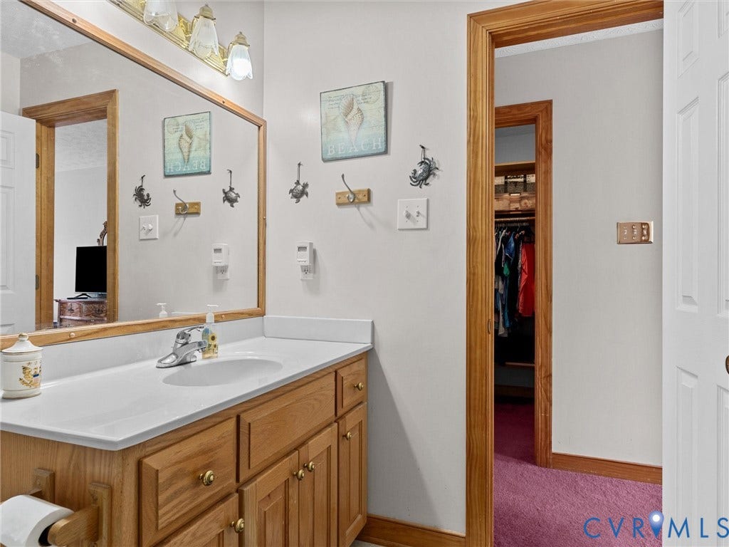 5325 Swift Hill Lane, Scandia Lake, Sandston, VA 23150 Wood-finish vanity with a white countertop and integrated sink, framed mirror, and warm-toned wood door trim
