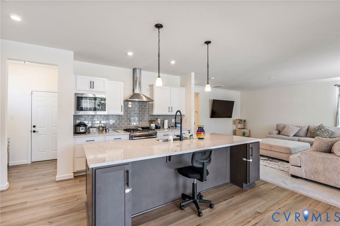 Kitchen island with quartz countertop, light wood-finish flooring, white cabinetry, stainless steel appliances, and a gray subway tile backsplash