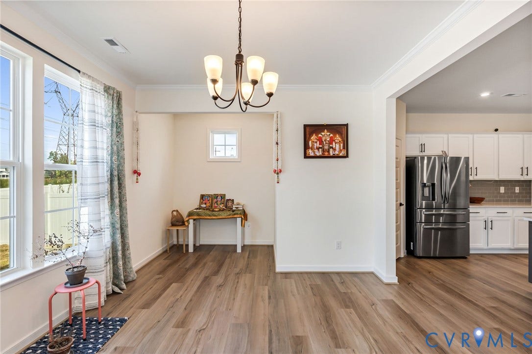 Spacious interior featuring wood-finish flooring, a contemporary chandelier, large windows, and an open-concept design to the kitchen with white cabinetry and stainless steel appliances
