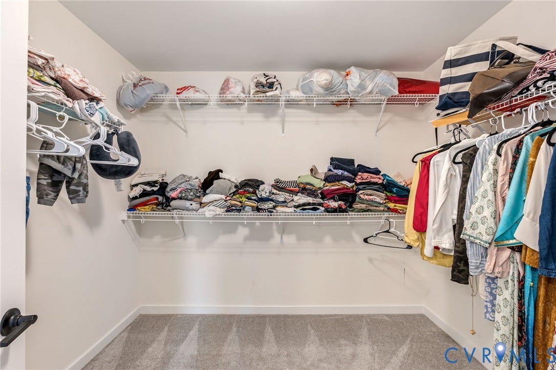 Spacious closet with light-colored carpeting, white wall finishes, and multiple levels of wire shelving and hanging rods
