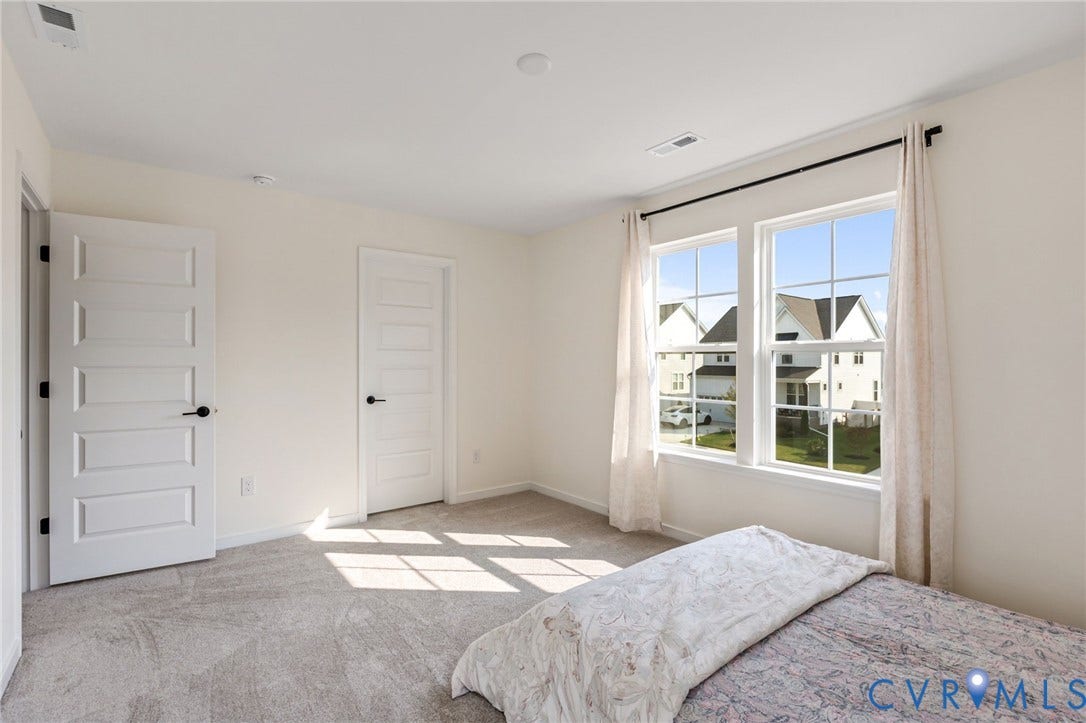 Neutral wall paint, two white paneled doors with matte black hardware, recessed ceiling lighting, two double-hung windows, and gray carpet