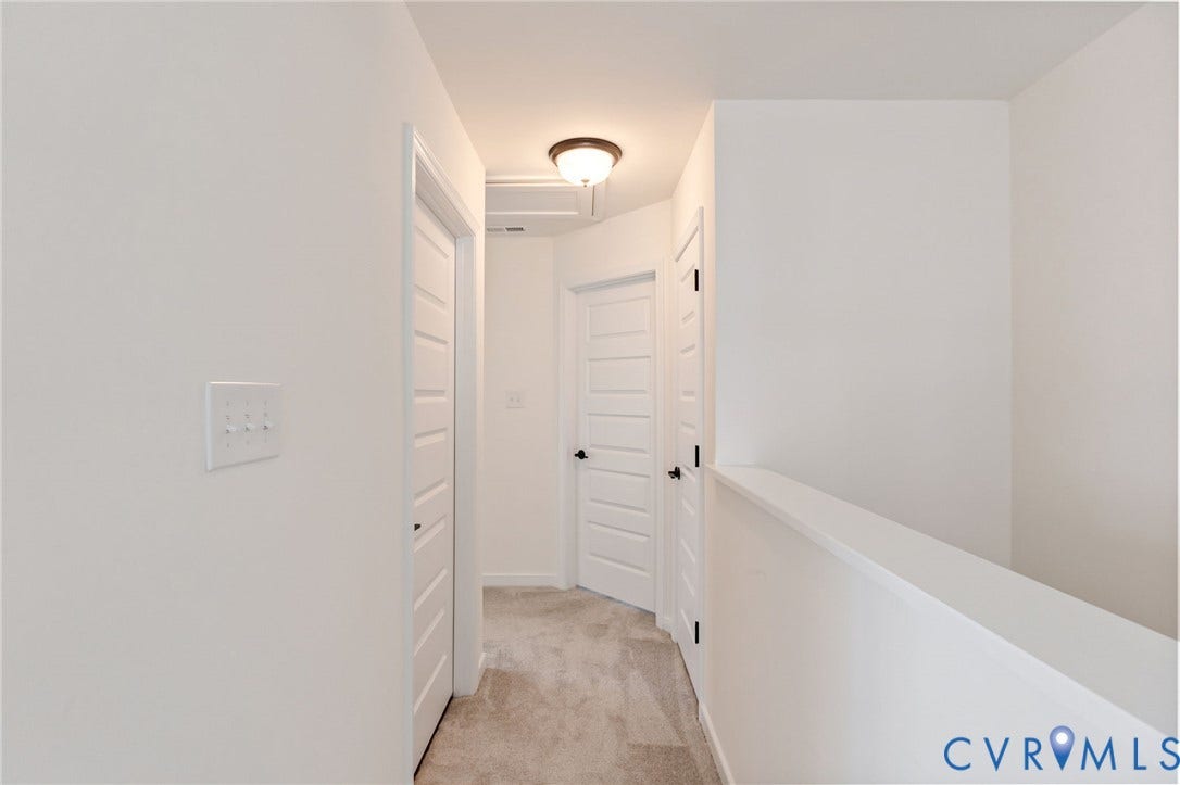 Neutral wall color, wall-to-wall carpeting, multiple panel doors with dark hardware, and flush mount lighting