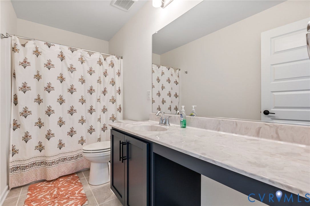 Vanity with integrated sink and chrome faucet, extensive countertop space, dark cabinetry with black hardware, and tiled flooring