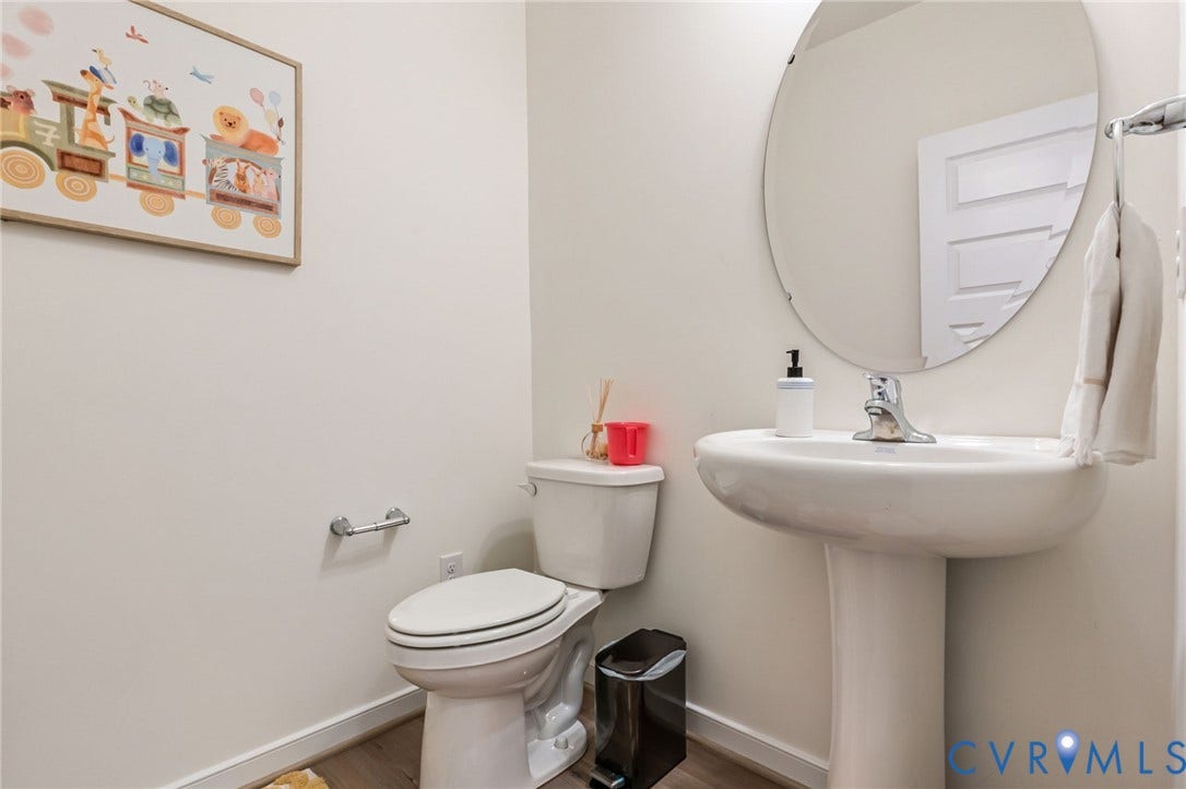 Pedestal sink with chrome faucet, oval frameless mirror, and wood-finish flooring