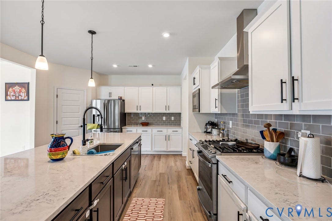 Kitchen featuring a large island with sink, stainless steel appliances, wood-finish flooring, white cabinetry, and subway tile backsplash