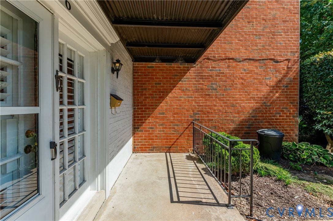 6 Stillwater Lane, Henrico, VA 23228 Entry door with grid-patterned glass, white painted brick exterior, red brick wall, covered entry, and metal handrail