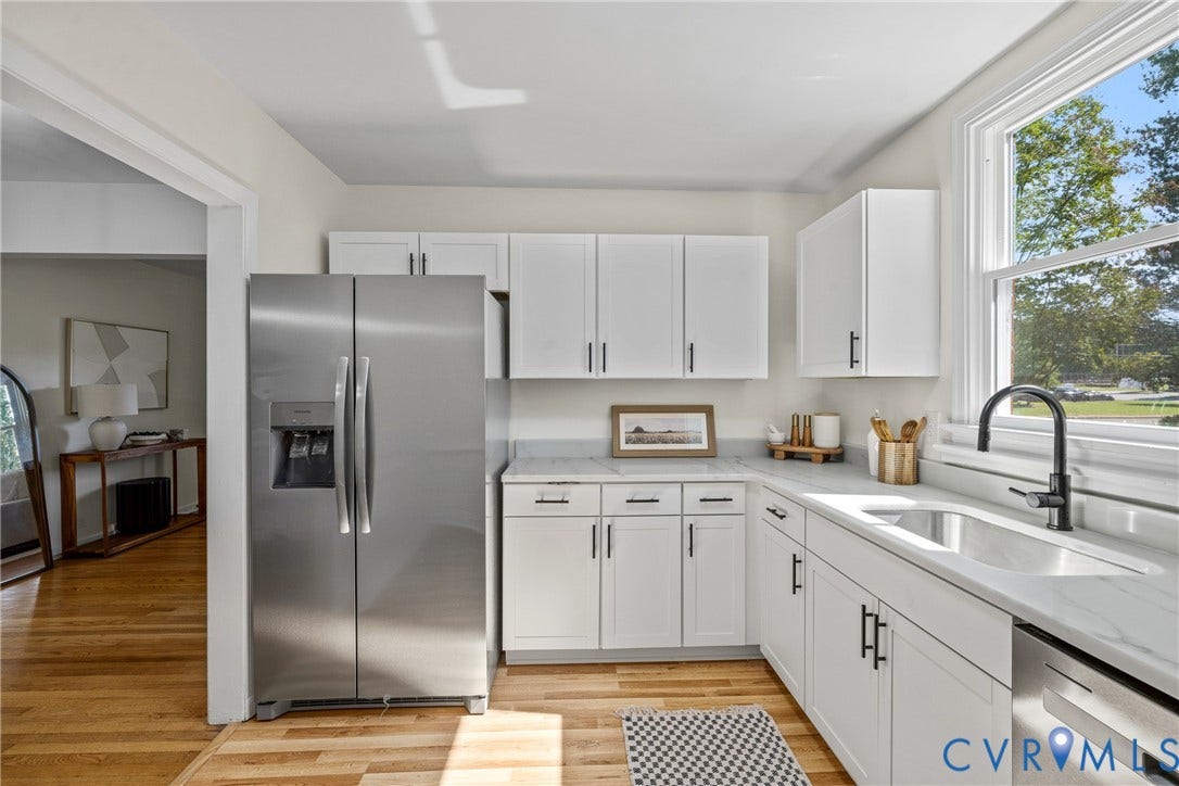 White cabinetry, stainless steel side-by-side refrigerator, under-mount stainless steel sink, black gooseneck faucet, and light-toned countertops