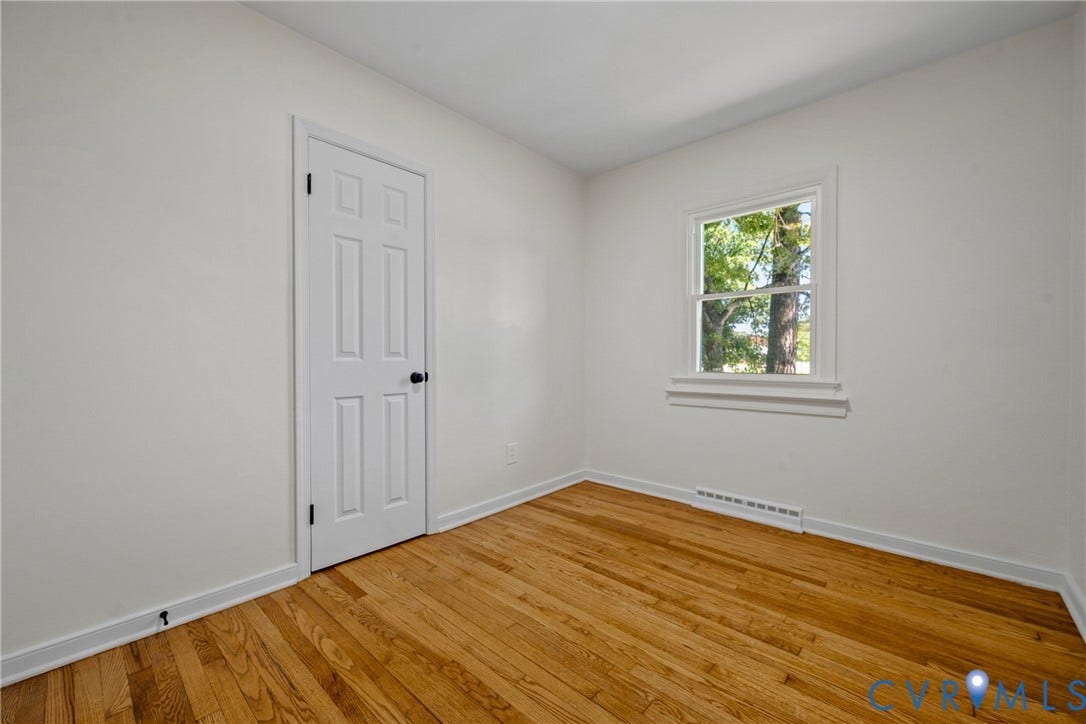 Wood flooring, white painted walls, white trim, white paneled door, and a single window