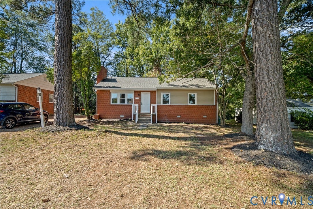 Brick and siding exterior, front entry with white railings, mature trees, and a sloped front yard
