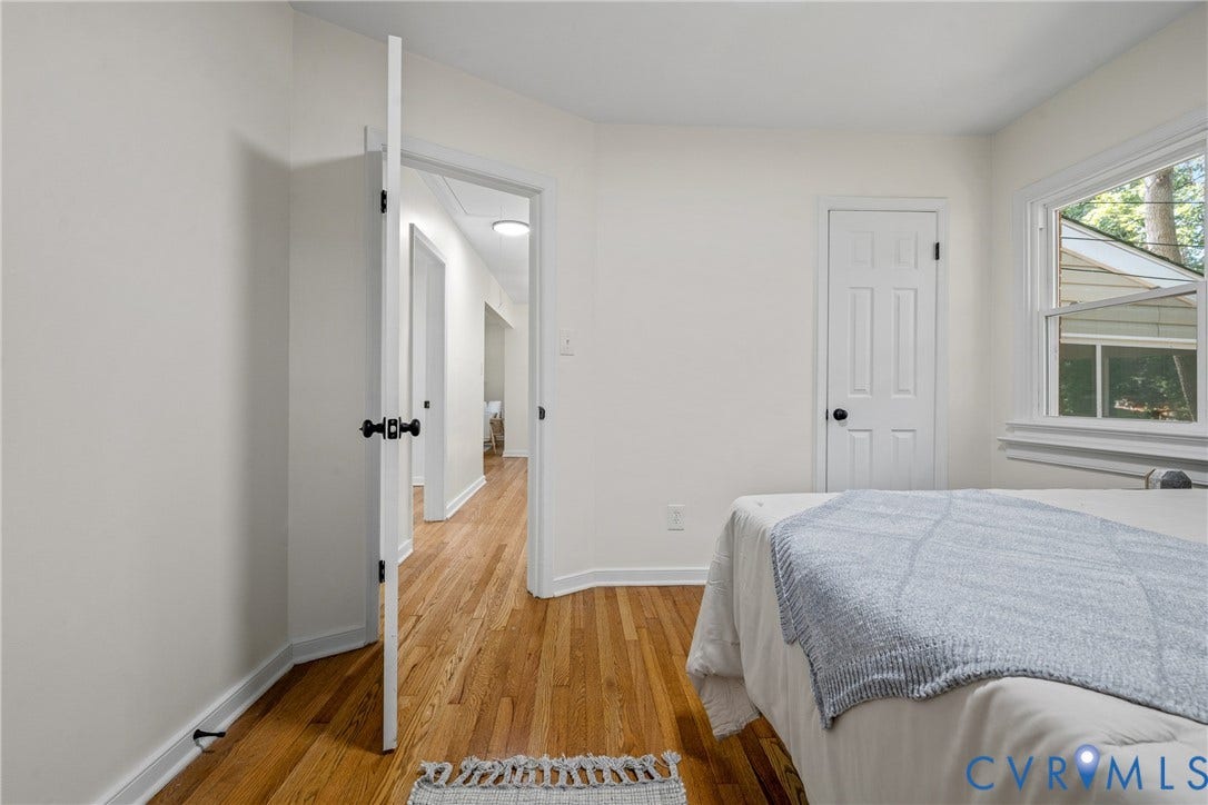 Hardwood flooring, white painted walls, white trim, white paneled door, and a single window