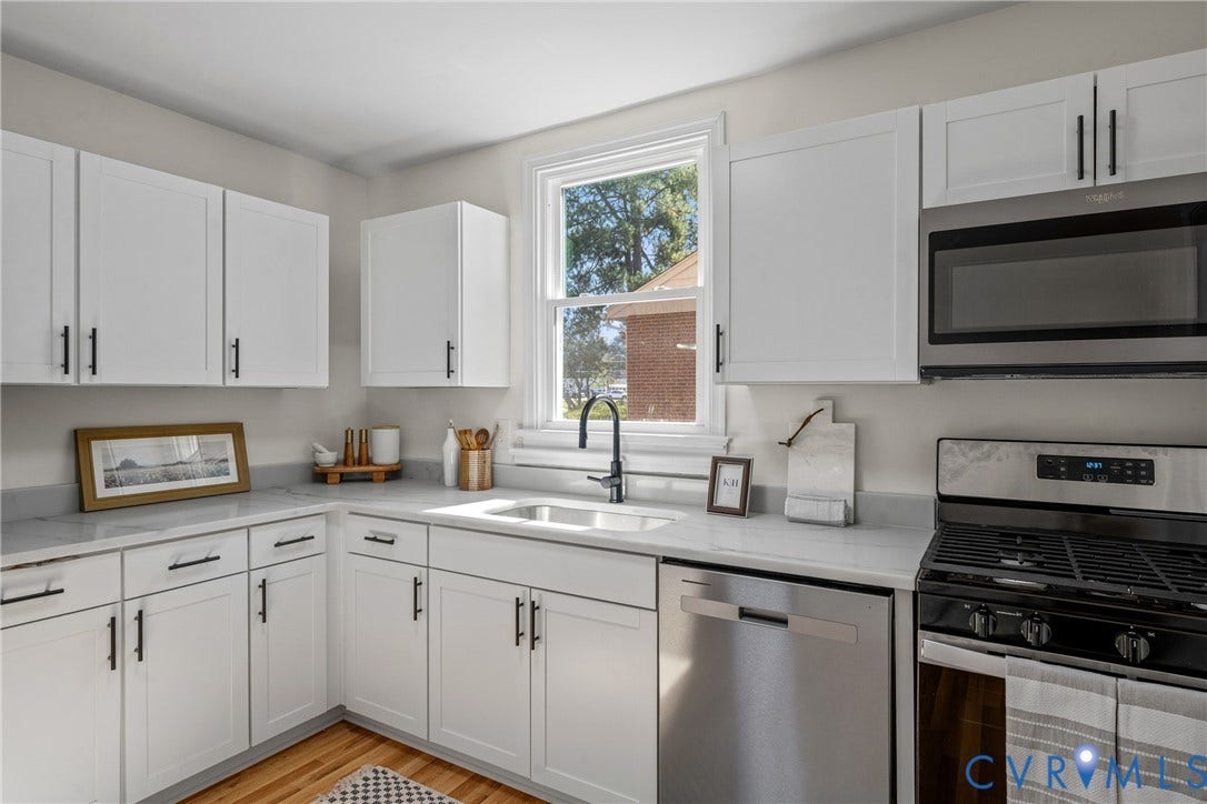 White shaker-style cabinetry with black hardware, stainless steel appliances, undermount sink with a black gooseneck faucet, light-toned countertops, and wood-finish flooring