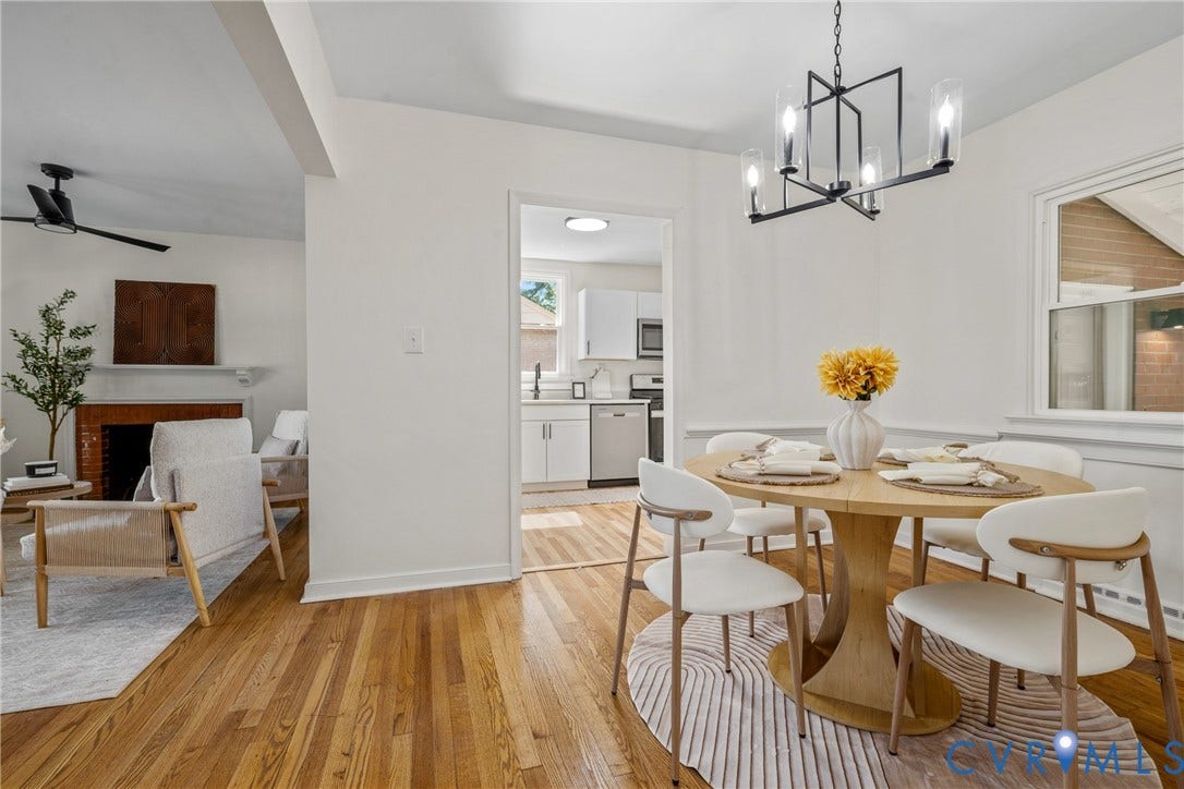 Hardwood flooring throughout, modern dining chandelier, white walls, kitchen with white cabinetry, and a fireplace with a wood mantel