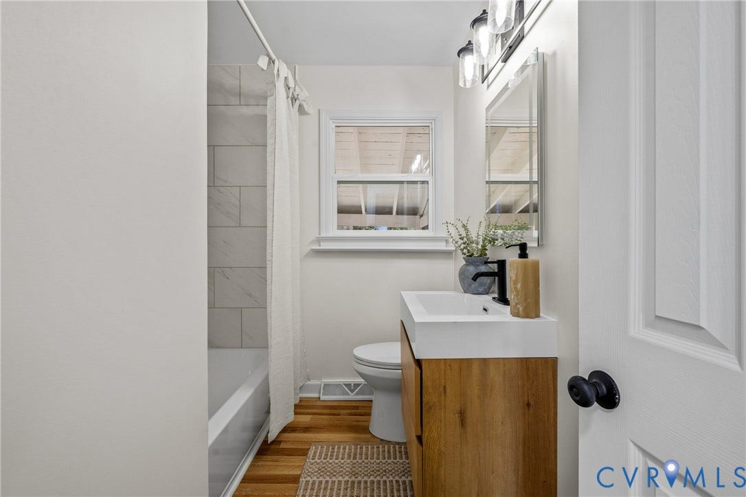 Wood-finish flooring, white vanity with integrated sink, matte black faucet, and clear glass vanity lighting