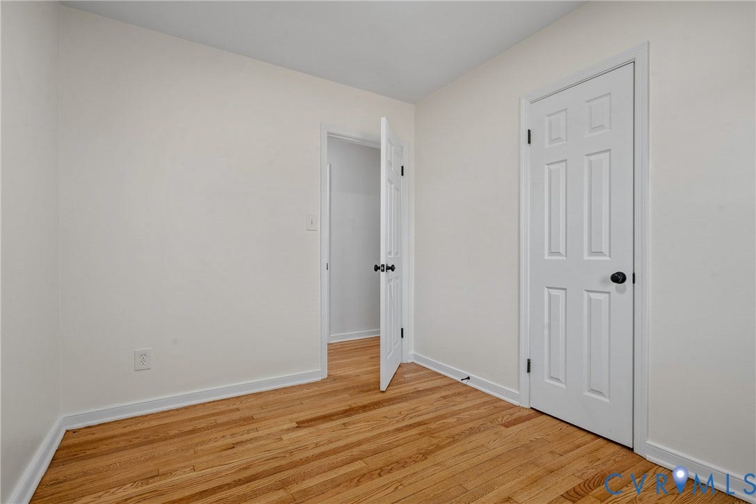 Hardwood flooring with a natural finish, white painted walls, and white paneled doors with dark hardware