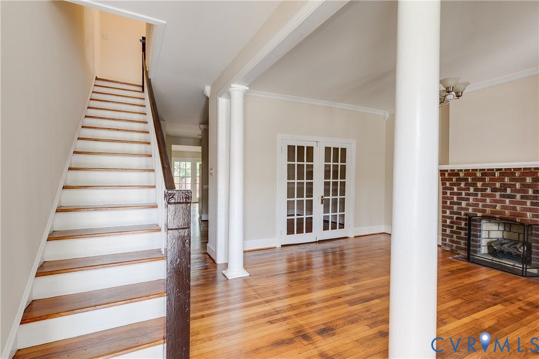 520 N 1st Street, Richmond, VA 23219 Hardwood flooring, brick fireplace surround with hearth, white French doors, decorative columns, and a staircase with wood treads
