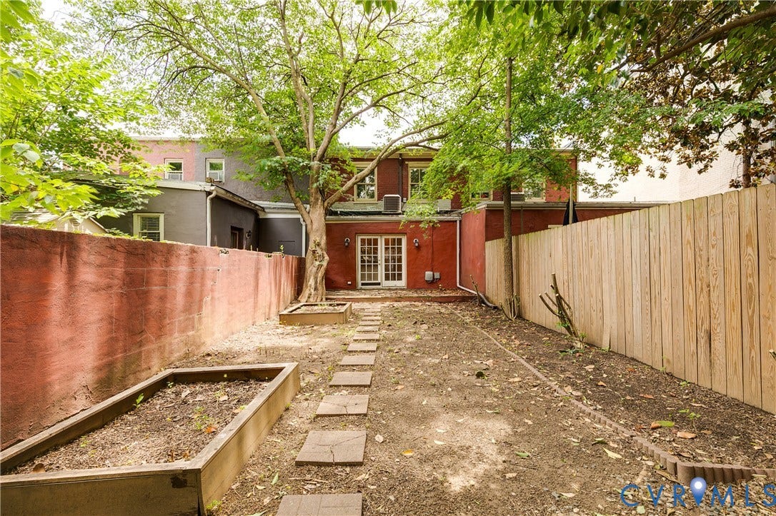 520 N 1st Street, Richmond, VA 23219 Enclosed backyard featuring a red privacy wall, natural wood fencing, a mature tree, and stone pavers