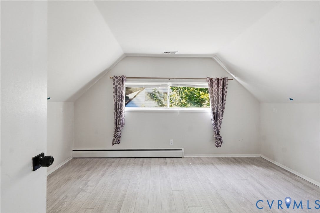 Sloped ceiling with recessed lighting, wood-finish flooring, and a single window