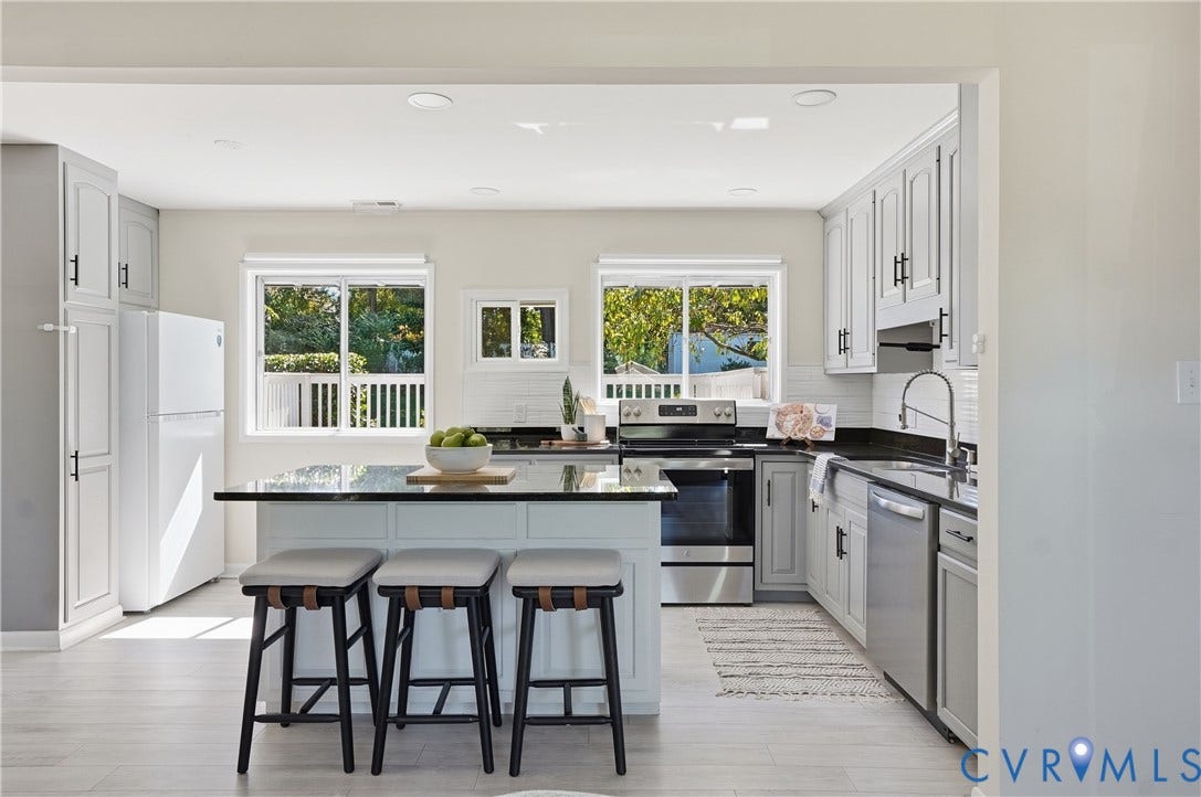 Kitchen featuring an island with seating, stainless steel appliances, white cabinetry with dark hardware, a tile backsplash, and light wood-finish flooring