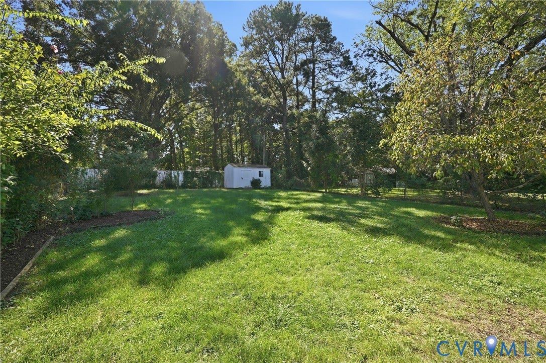Expansive green lawn with mature trees, bordered by a white privacy fence and a dedicated garden bed