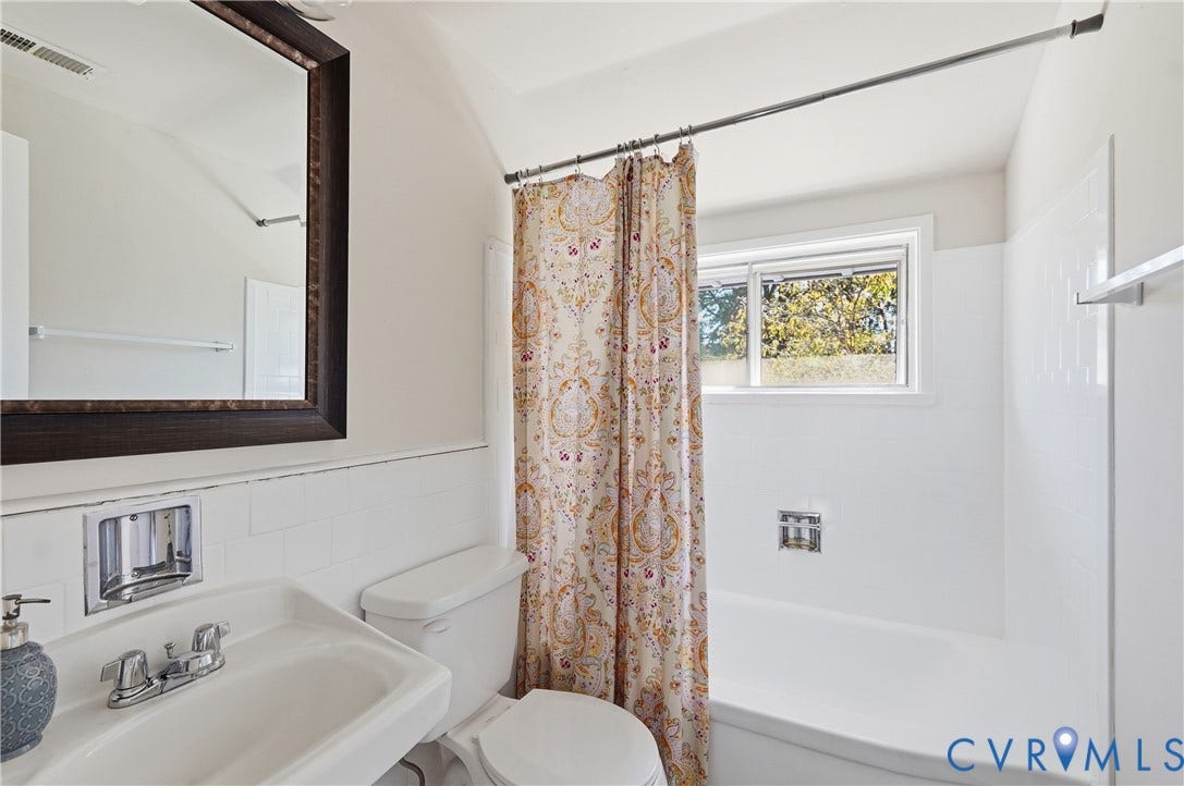 White subway tile wainscoting, framed vanity mirror, and a built-in tub with a sliding window