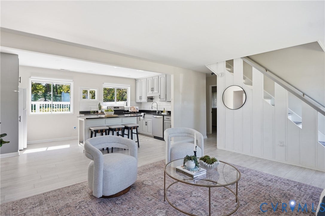 White wood-finish flooring throughout, open-concept living area, white cabinetry, dark countertops, and stainless steel appliances