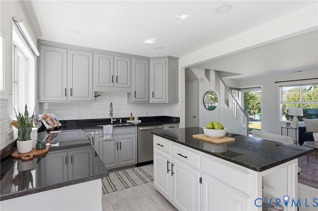 Kitchen featuring an island, black countertops, stainless steel appliances, a tile backsplash, and light-colored cabinetry