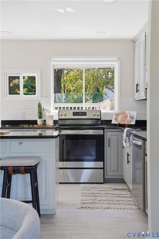 Light wood-finish flooring, white subway tile backsplash, stainless steel range, and black countertops