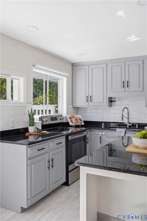 Kitchen featuring gray cabinetry, dark countertops, white subway tile backsplash, stainless steel appliances, and wood-finish flooring