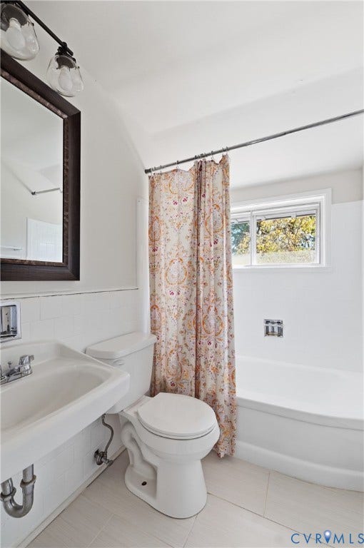 Bathroom featuring a wall-mounted sink, white bathtub, and a window providing natural light