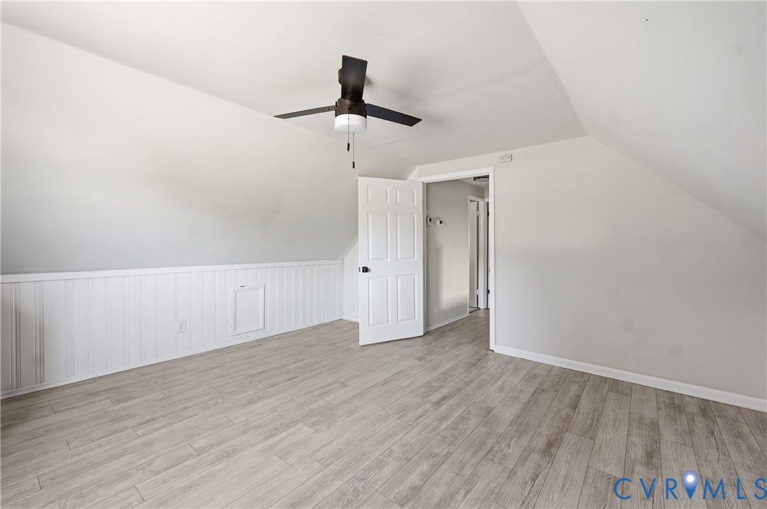 Sloped ceilings with a ceiling fan, plank-style flooring, white paneling, and a white interior door
