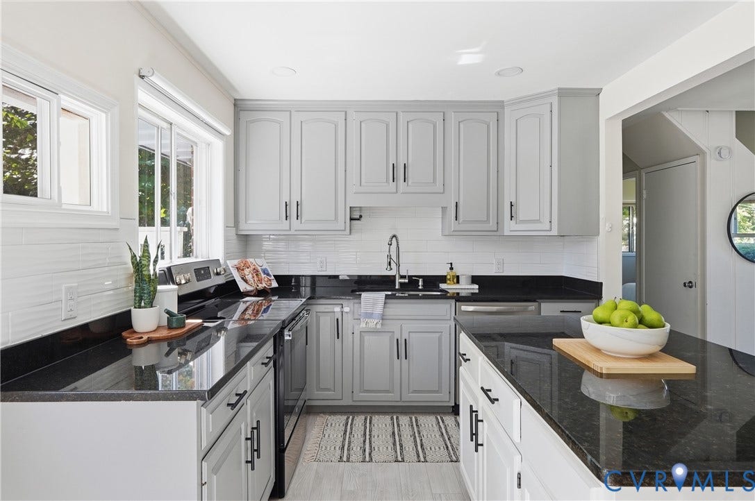 Light gray cabinetry with black hardware, black stone-finish countertops, white subway tile backsplash, and stainless steel appliances