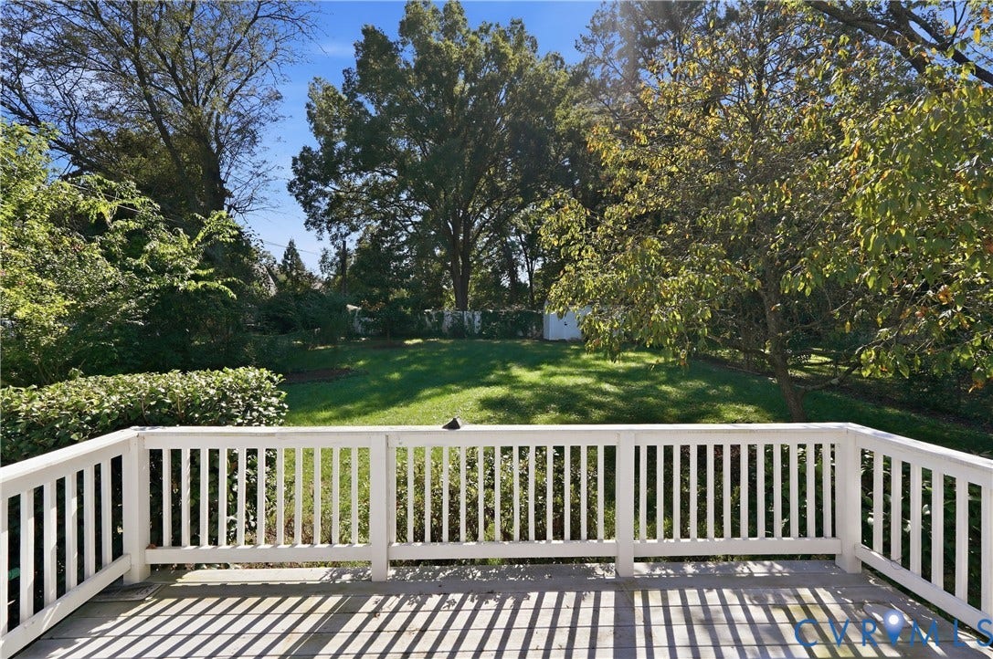 Spacious deck with white balustrade railing overlooking a verdant lawn and mature trees