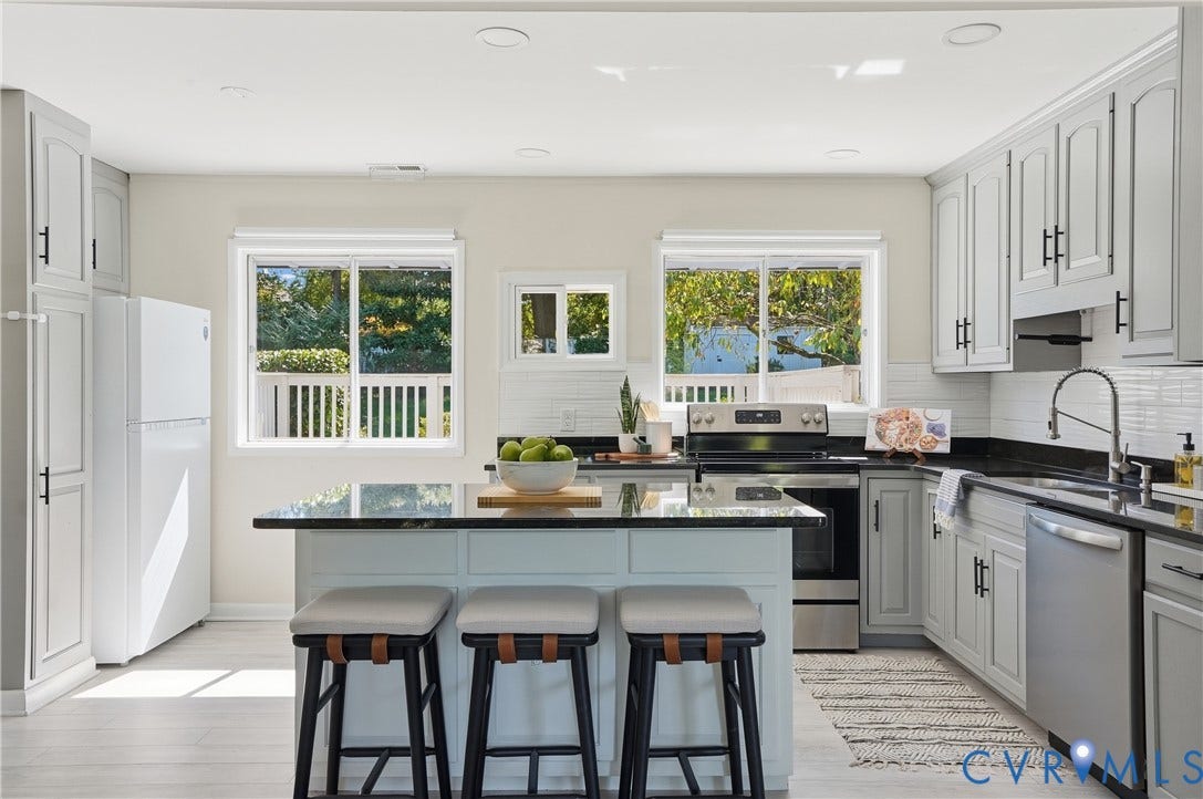 Kitchen featuring light gray cabinetry, white subway tile backsplash, black countertops, and stainless steel appliances