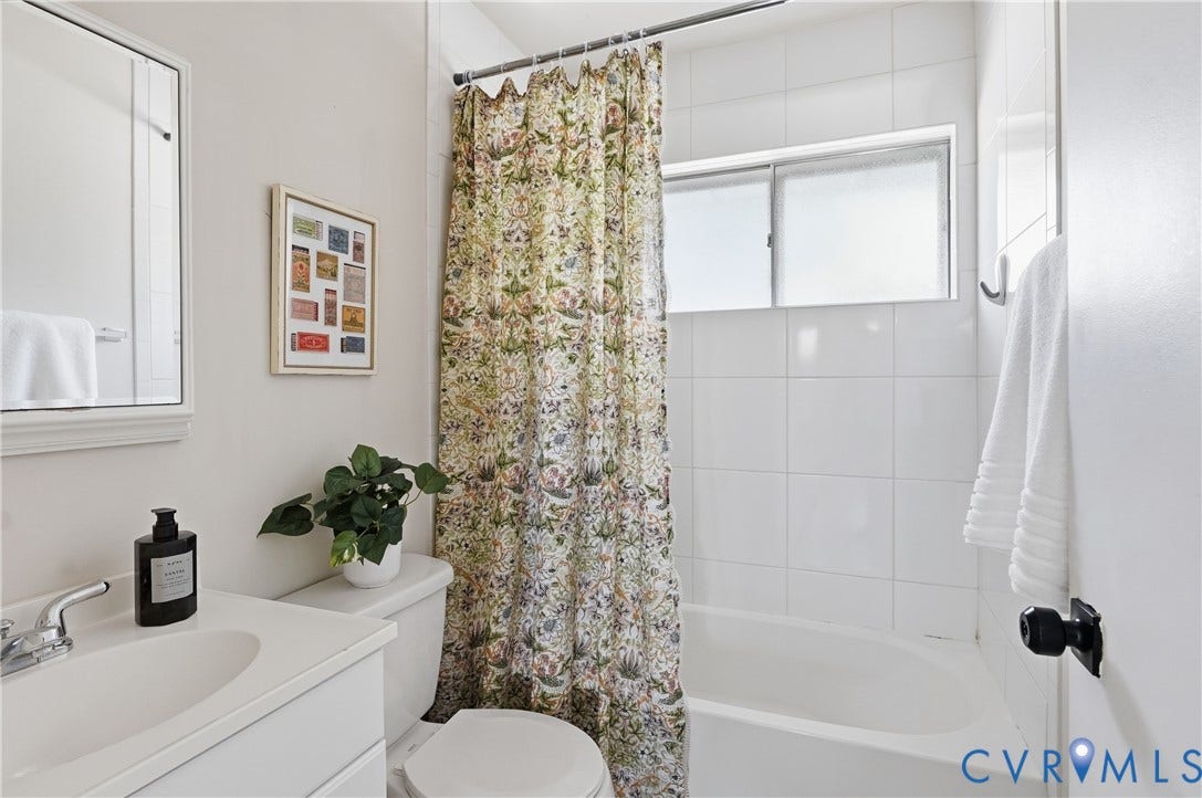 Bathroom featuring a white vanity with integrated sink, chrome faucet, white toilet, white tiled bathtub surround, and a frosted window