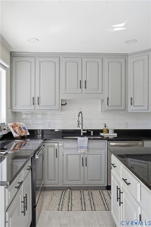 Kitchen featuring light-toned cabinetry with dark hardware, dark countertops, and a white subway tile backsplash