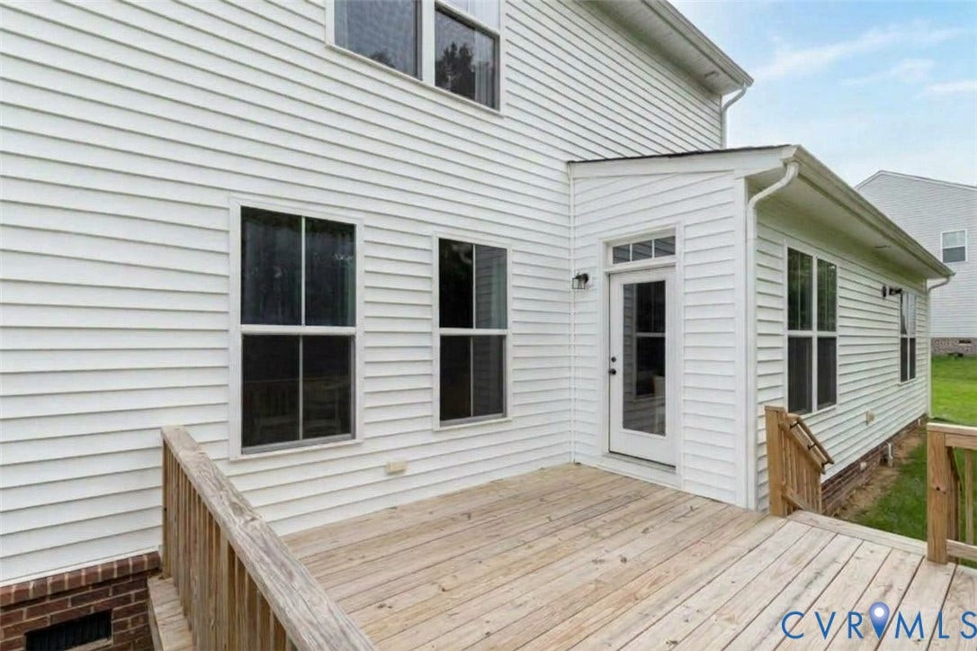 Spacious wood-finish deck with railing, white panel siding, and multiple windows
