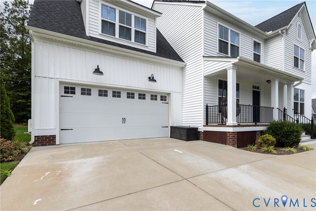White siding exterior with a dark shingle roof, concrete driveway, attached two-car garage, and a covered porch with black railings