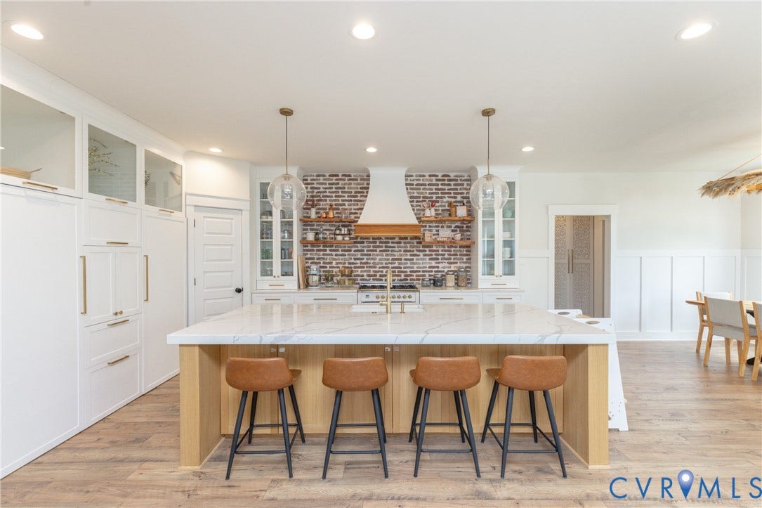Expansive kitchen island with a stone countertop, custom wood cabinetry, a brick accent wall, built-in range, and wood-finish flooring