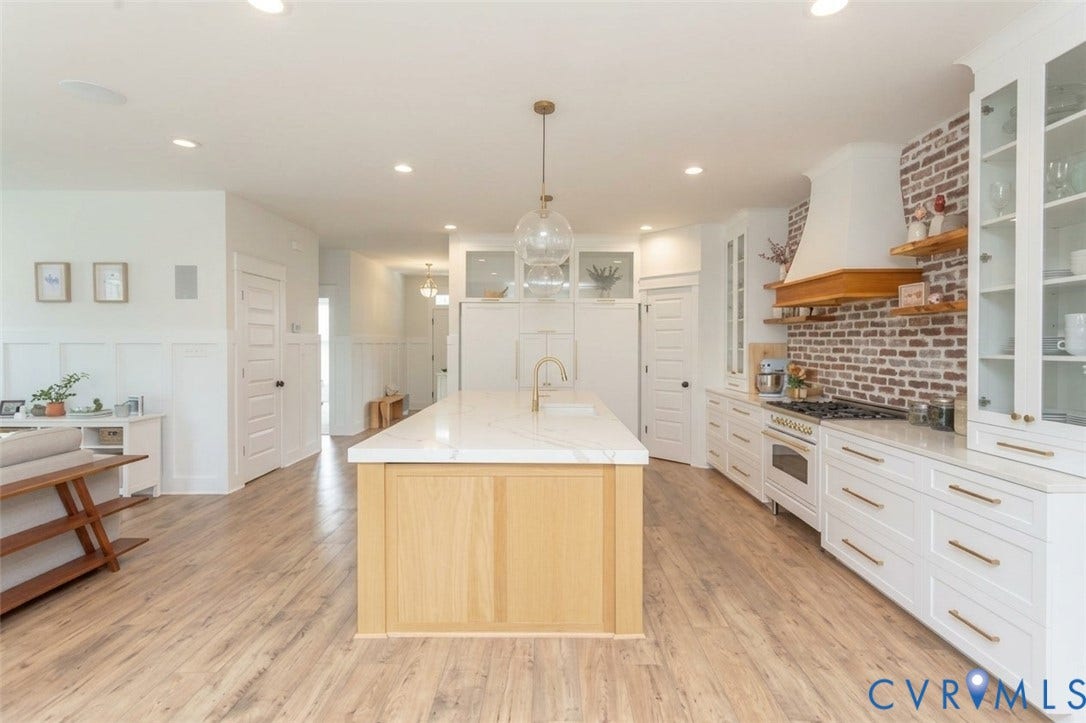 Gourmet kitchen featuring a central island with a stone countertop, white cabinetry with brass-finish hardware, a brick-finish backsplash, and wood-finish flooring