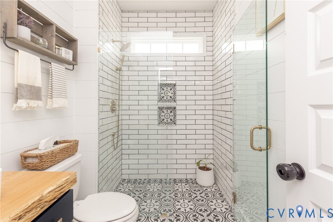 Subway tile shower with decorative accent niches, patterned floor tile, and a glass enclosure with a brass handle