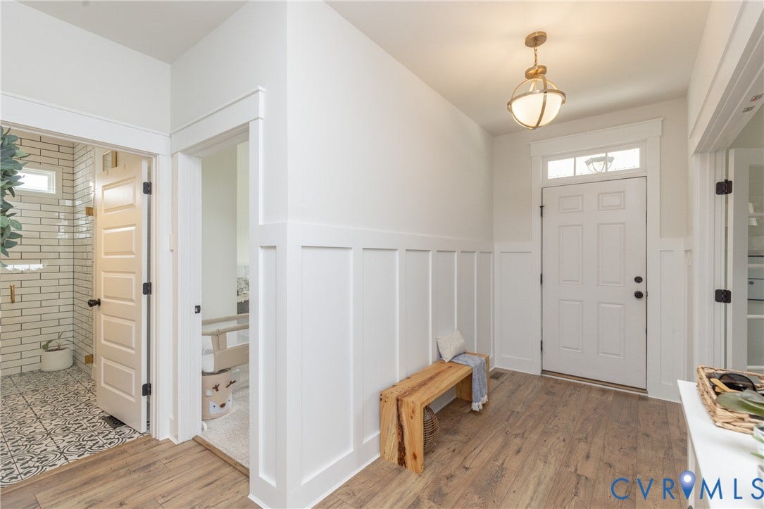Entryway featuring wood-finish flooring, white paneled walls, and a transom window above the entry door