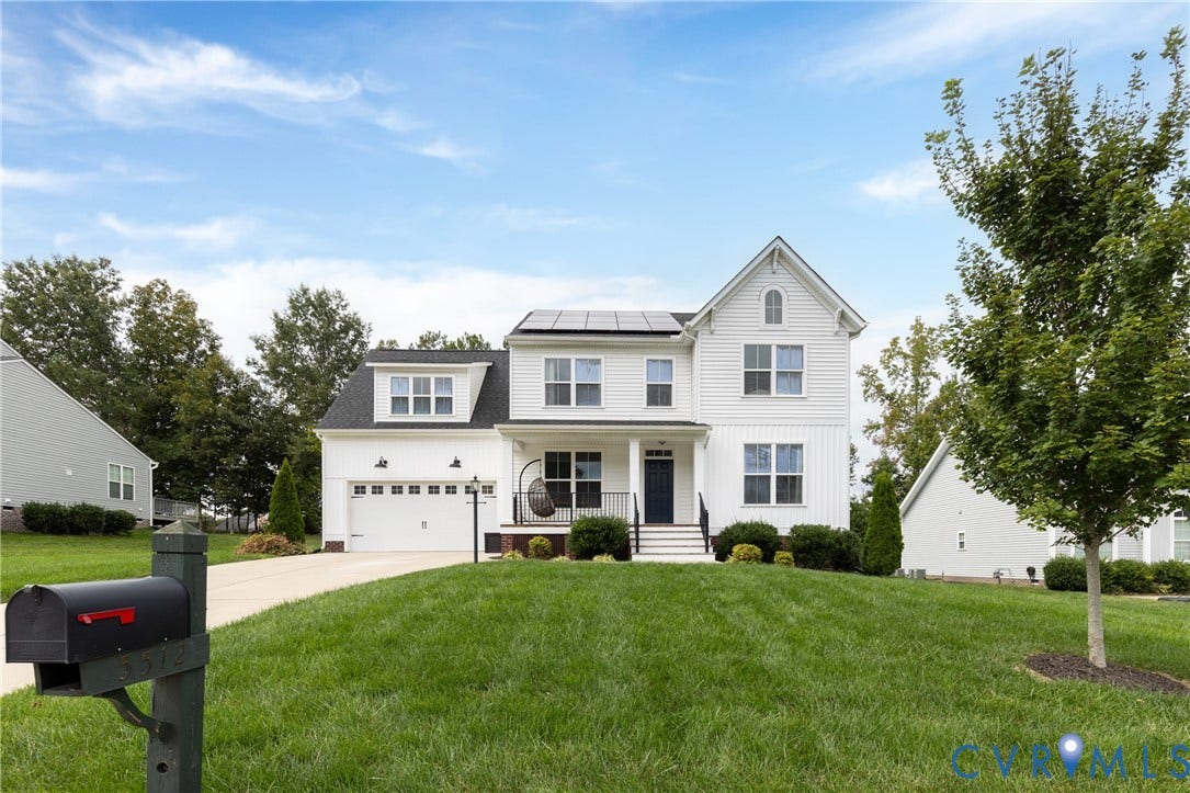 White siding exterior with black accents, front-facing two-car garage, mature landscaping, and a well-maintained lawn