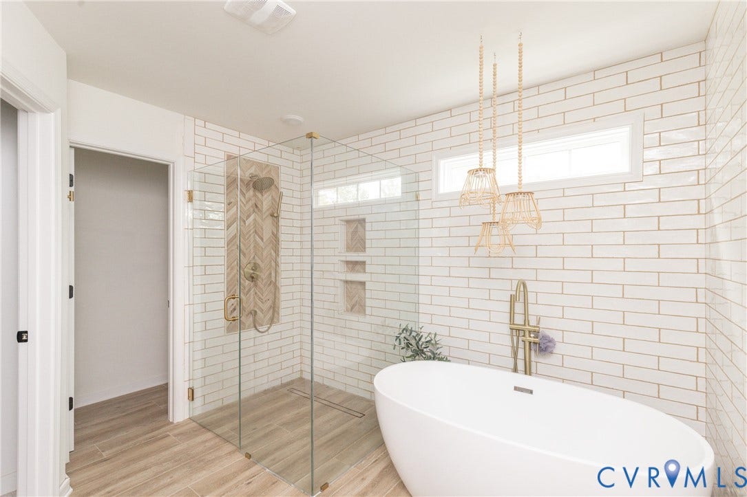 Freestanding soaking tub, glass-enclosed shower with herringbone tile accent, wood-finish flooring, and white subway tile walls