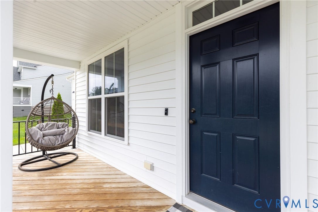 Covered front porch with wood-finish flooring, white siding, and a paneled entry door with transom window